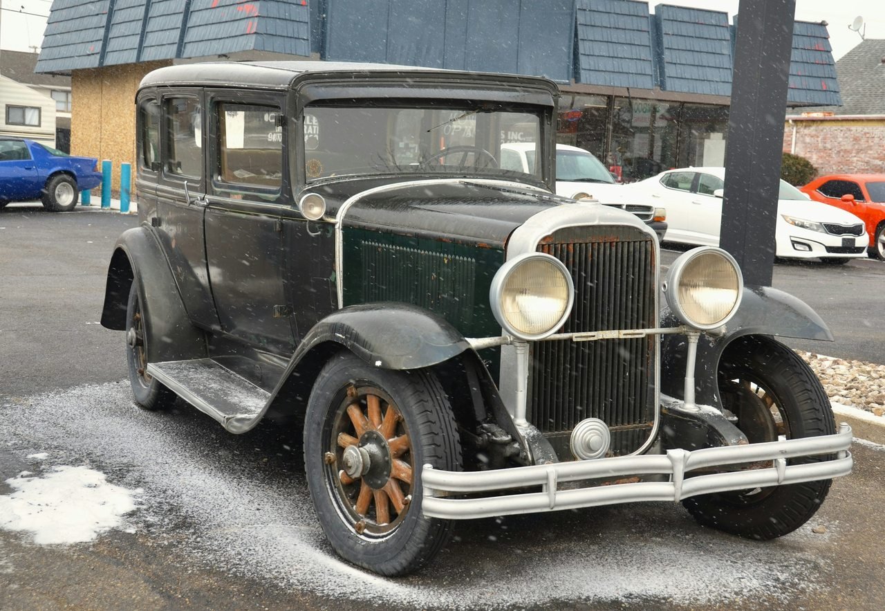Dark antique sedan with upright grille, round headlamps, and running boards.