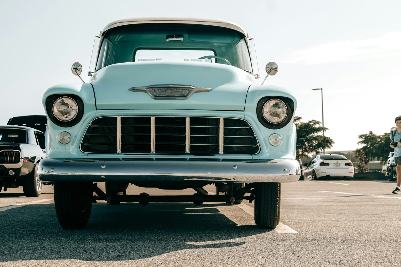 Pale blue classic pickup truck viewed from the front at a car gathering.